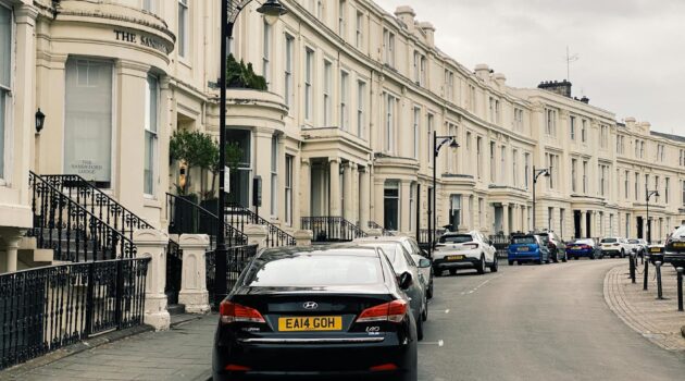 a row of typical british townhouses with cars parked along the street